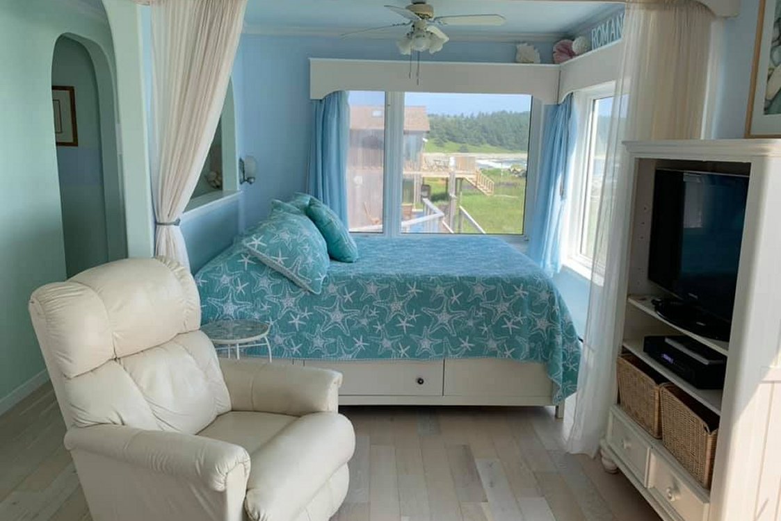 Bedroom with queen bed, leather chair, and wrap around windows with a spectacular beach view