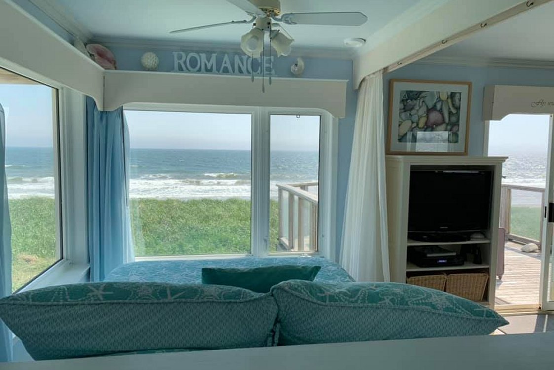 View of ocean waves through large windows from the SeaSpray Suite queen bed