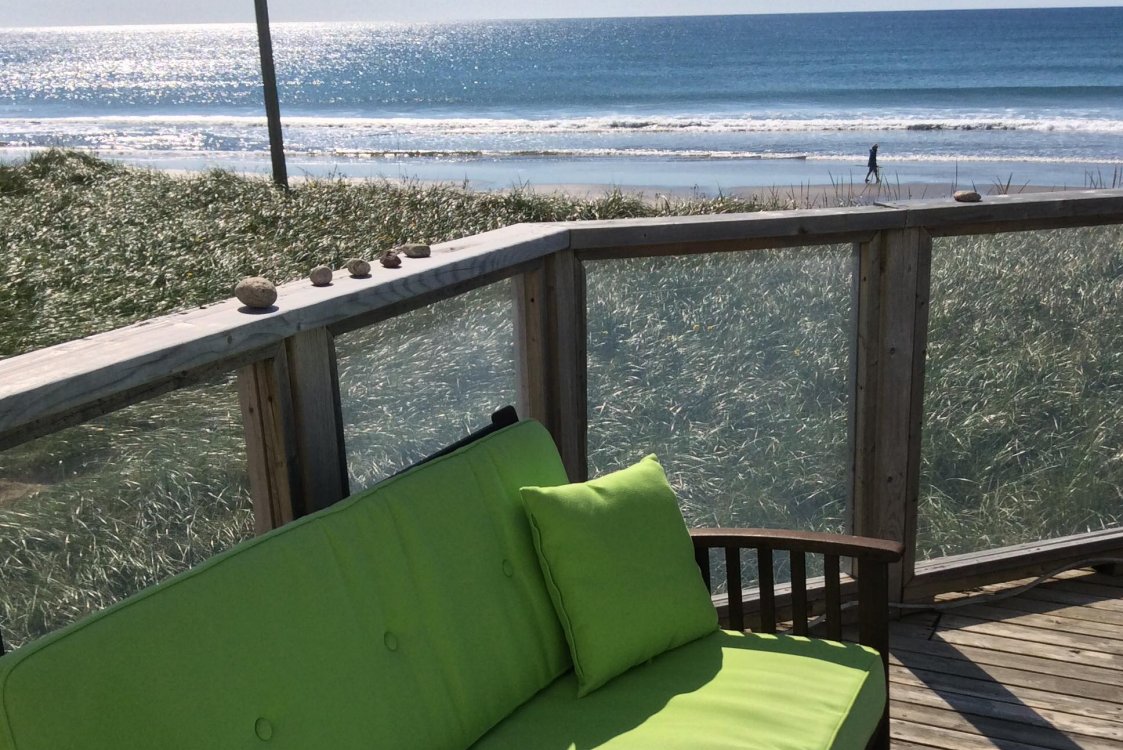 Sea Spray Deck, with seating, glass railing, and view of the beach, waves and sunshine on the water